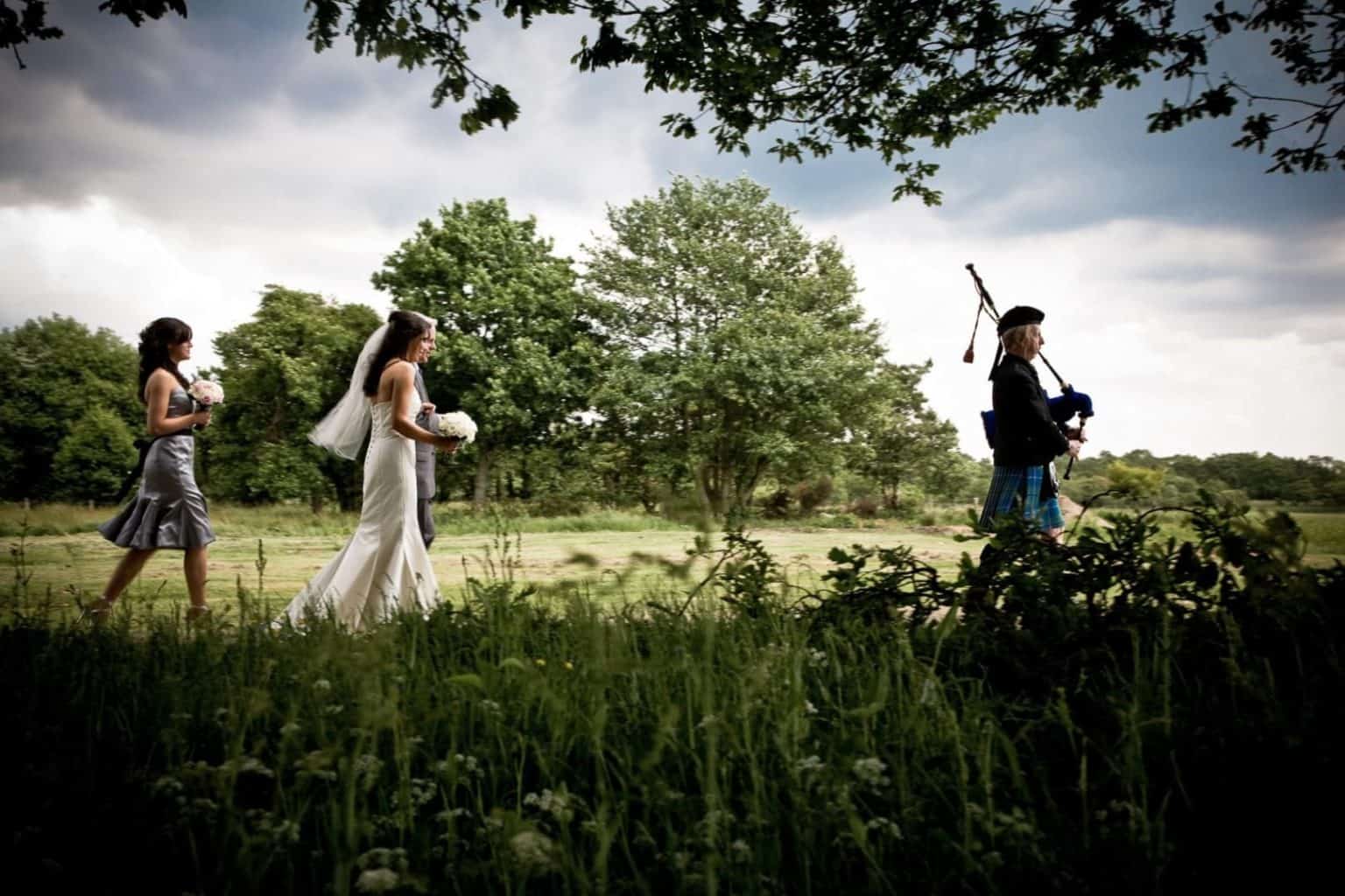 a-loch-lomond-wedding-(1-of-1) a bride is led by the piper to her outdoor wedding in loch lomond