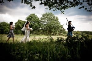 a bride is led by the piper to her outdoor wedding in loch lomond