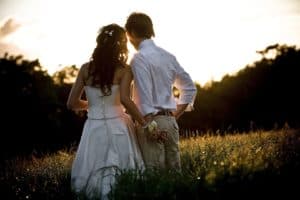 a couple stand in a field during sunset on their wedding day