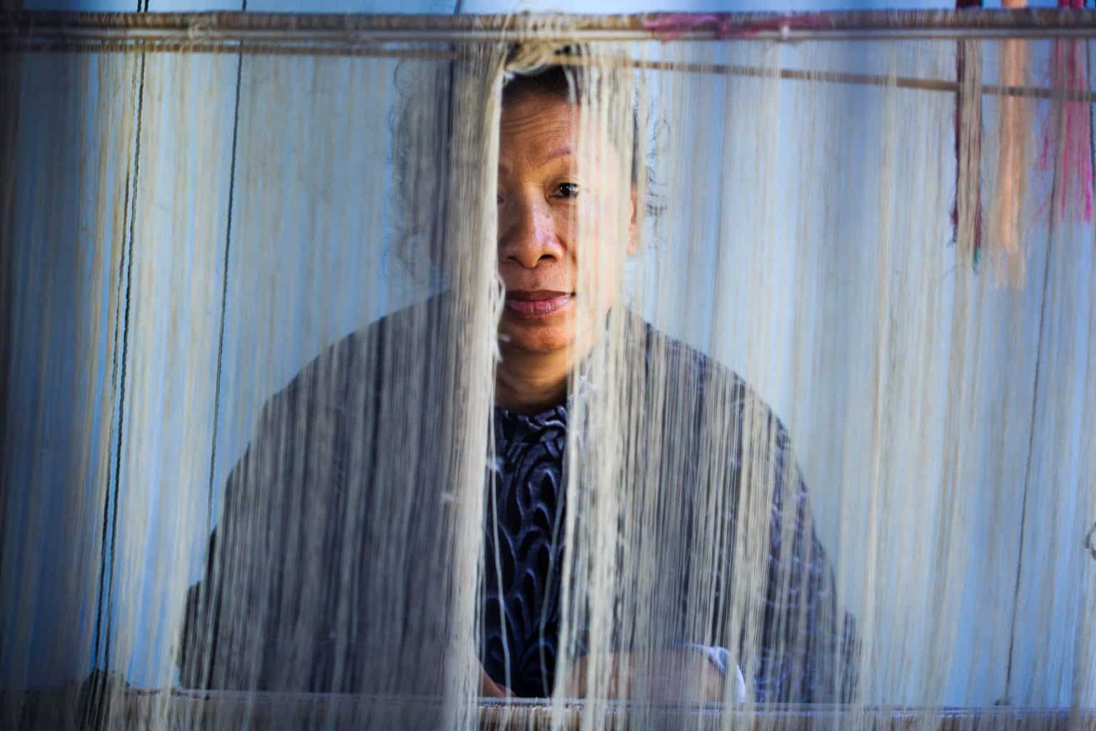 laos-woman-making-silk a laos woman looks through the threads of her loom where she is making silk