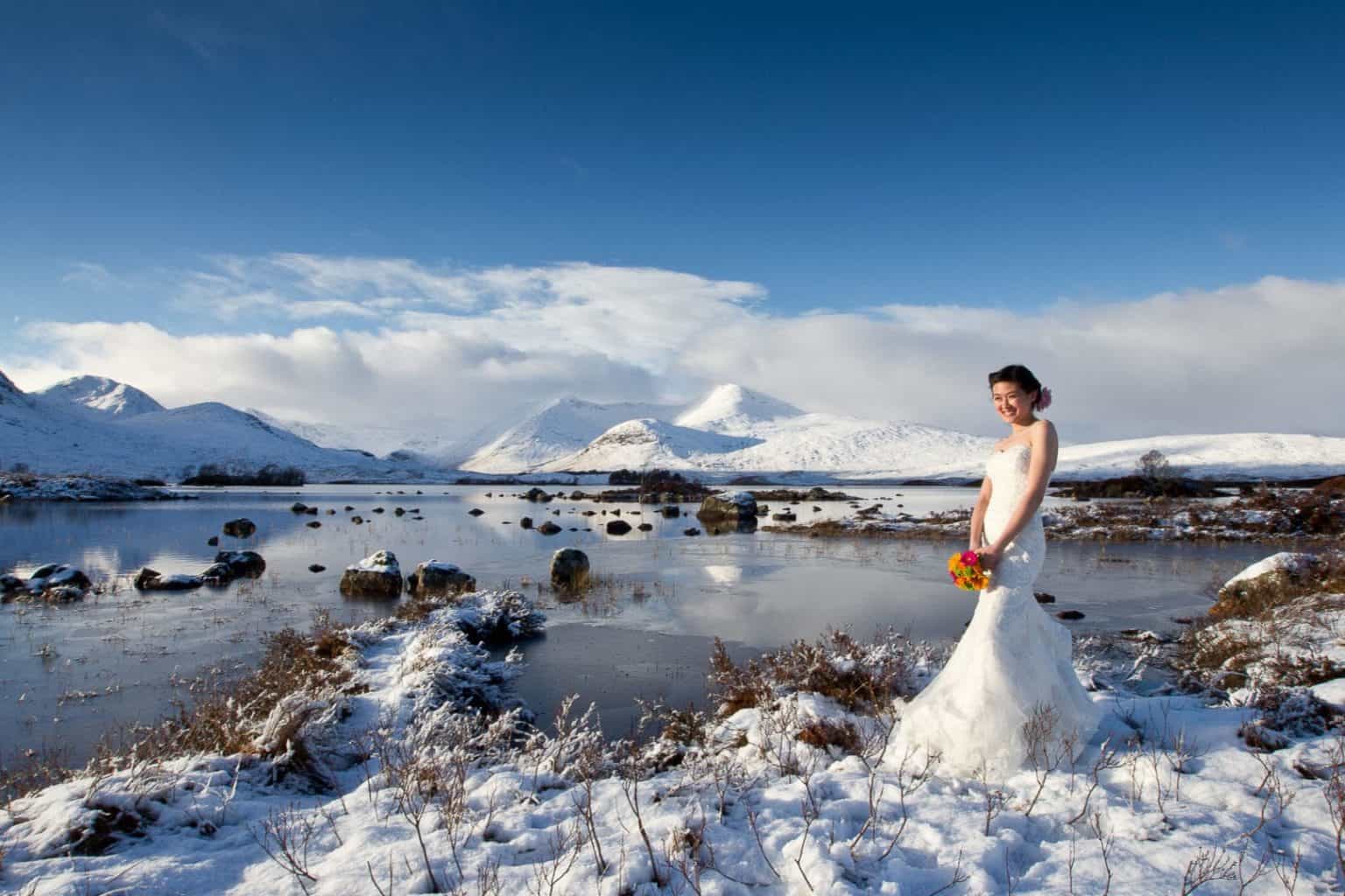 scotland-winter-wedding an bride stands in the snow by loch rannoch in scotland
