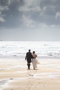 a bride and groom walk on a beach in lewis on their wedding day