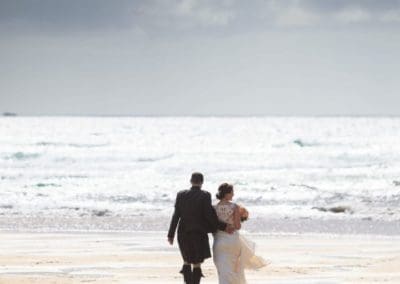 a bride and groom walk on a beach in lewis on their wedding day