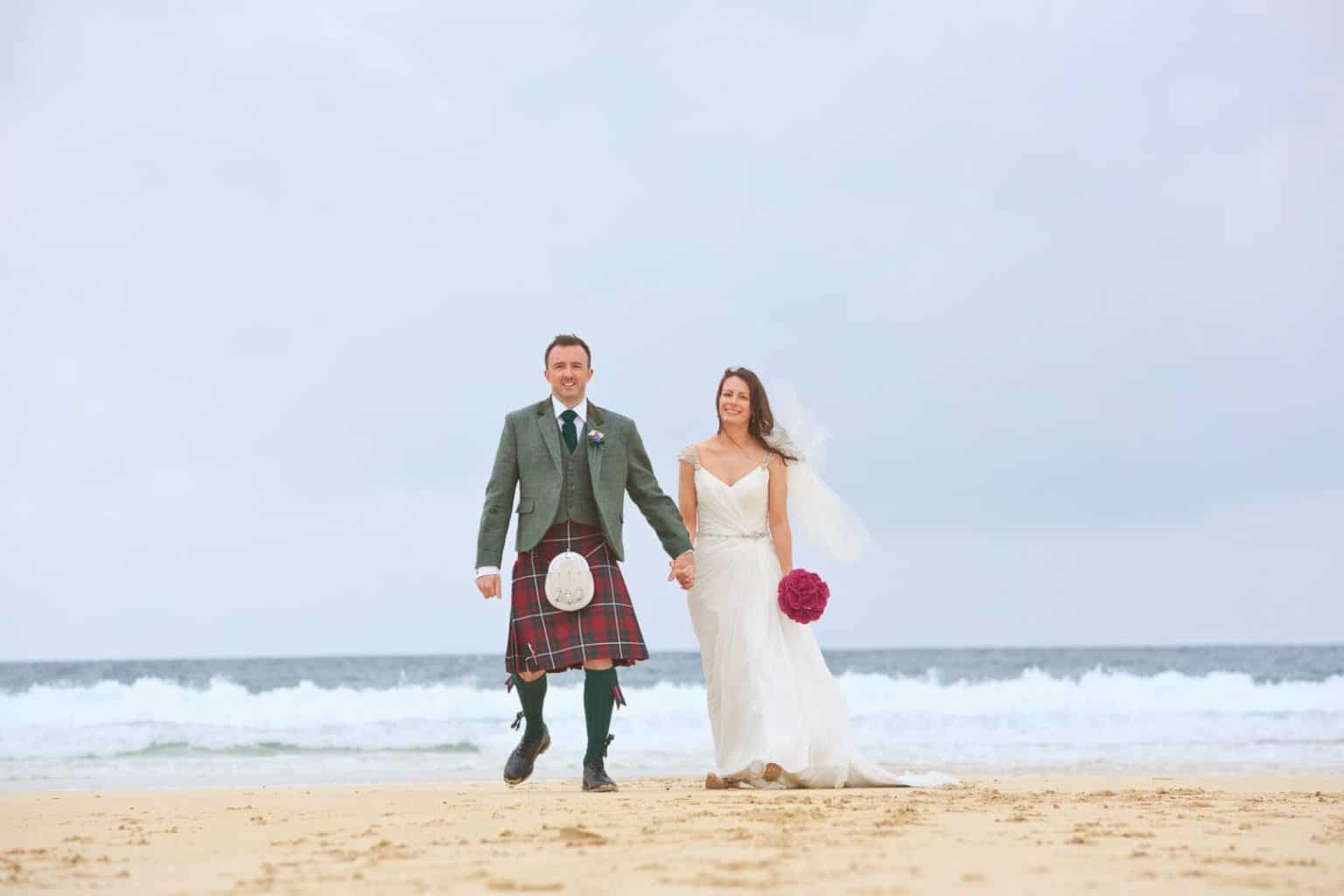 talla-na-marra-wedding-photograph a bride and groom in a kilt walk along a beach on the isle of harris on their wedding day