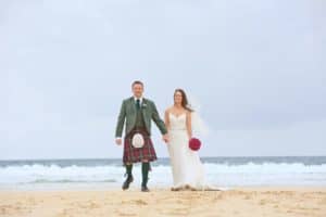 a bride and groom in a kilt walk along a beach on the isle of harris on their wedding day