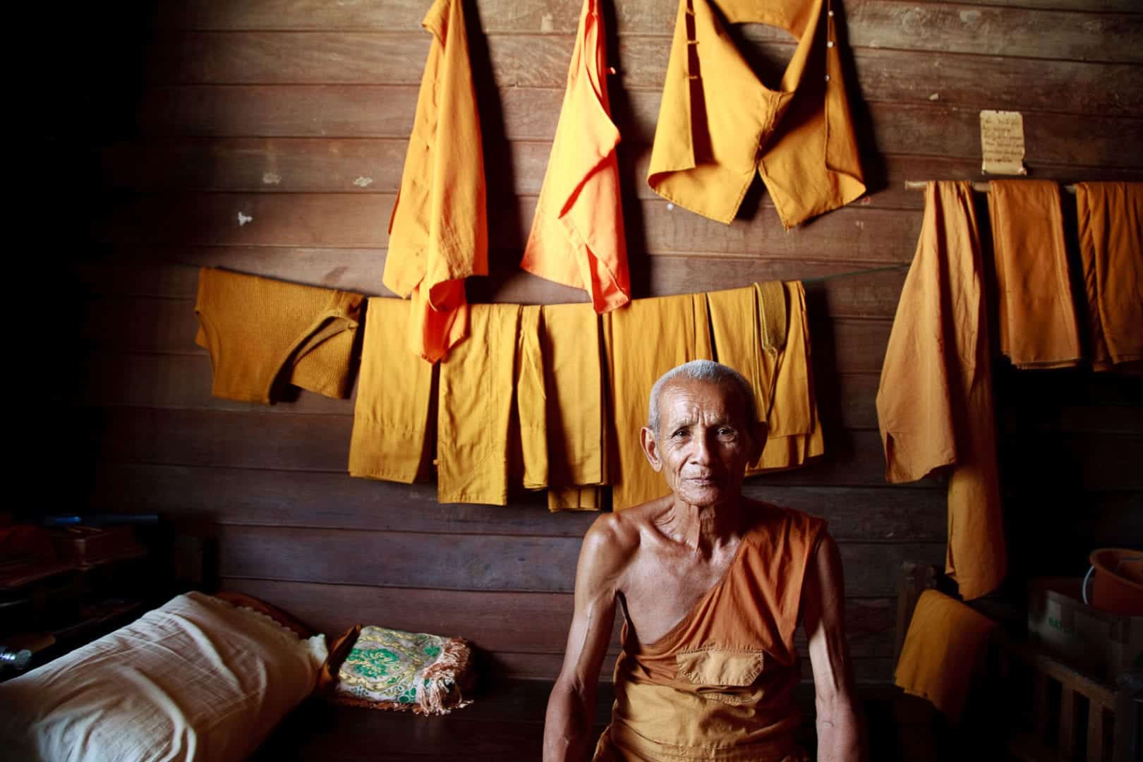 a thai monk sits on his bed in his monastery