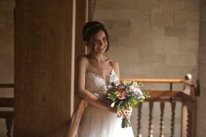 Achnagairn Castle bridge, wearing a white wedding dress and holding a bouquet of flowers